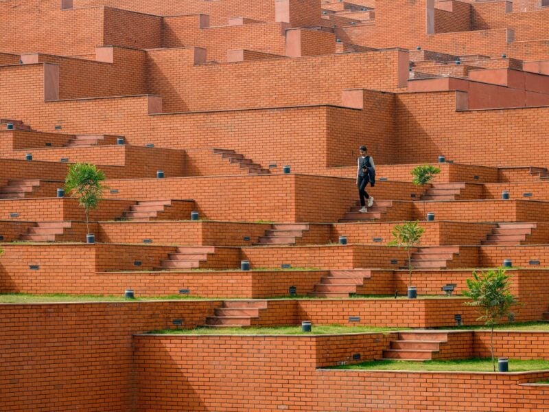 A woman walks among the steps forming the building of Prestige University by Sanjay Puri Architects