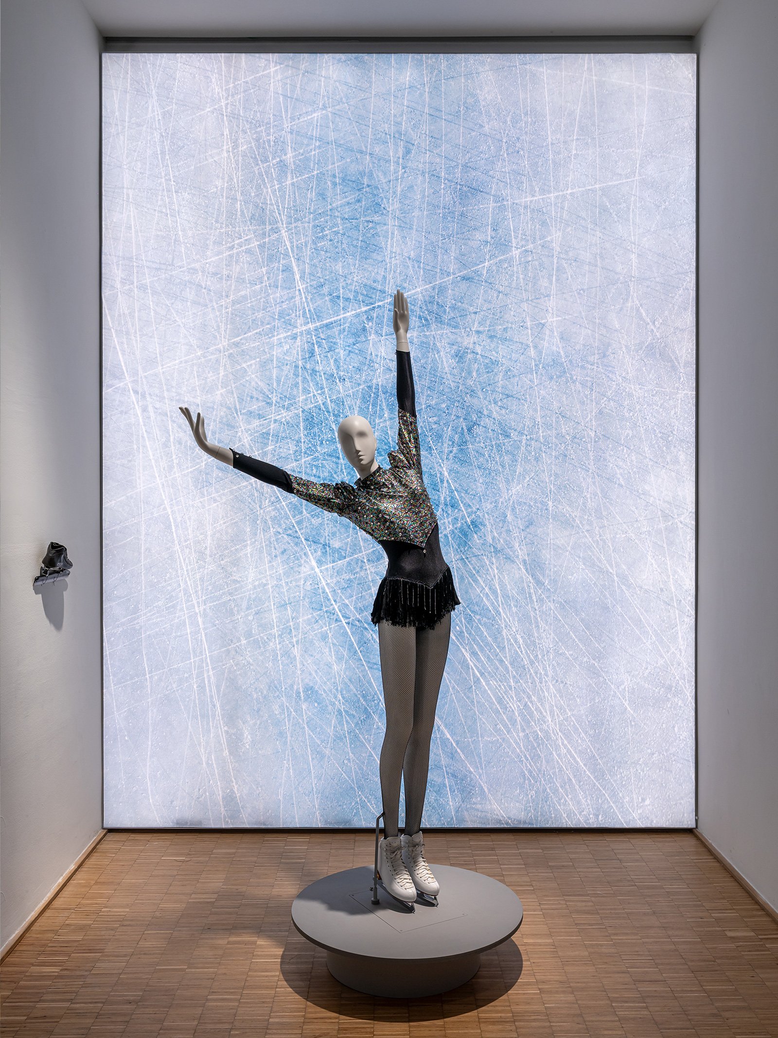 A mannequin wears an ice skating costume against a glowing wall that resembles the surface of a rink in the Triennale winter sports exhibition White Out.