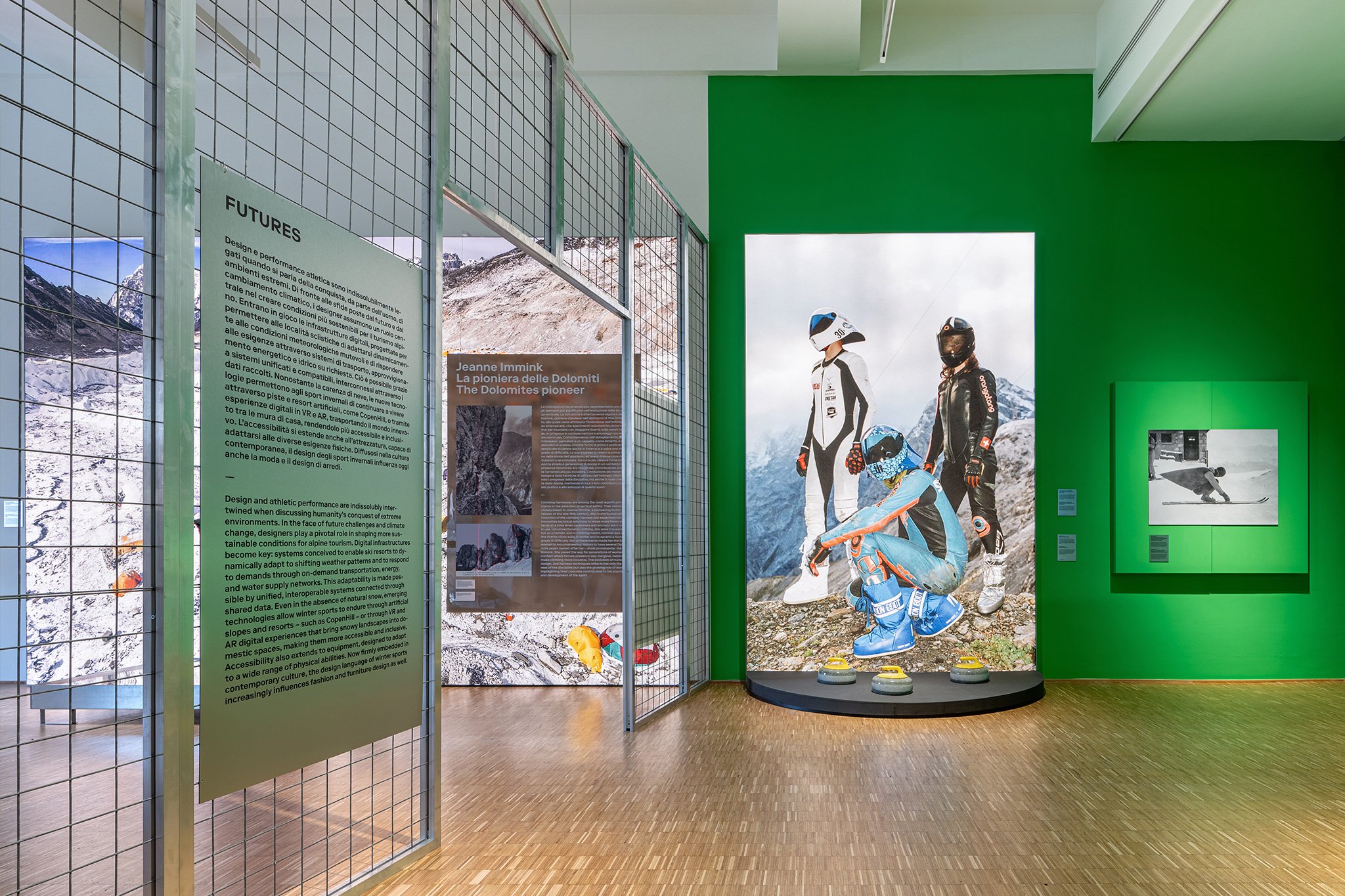 A view of White Out a Triennale winter sports exhibition featuring a display of curlers with three curling rocks shown against a green wall.