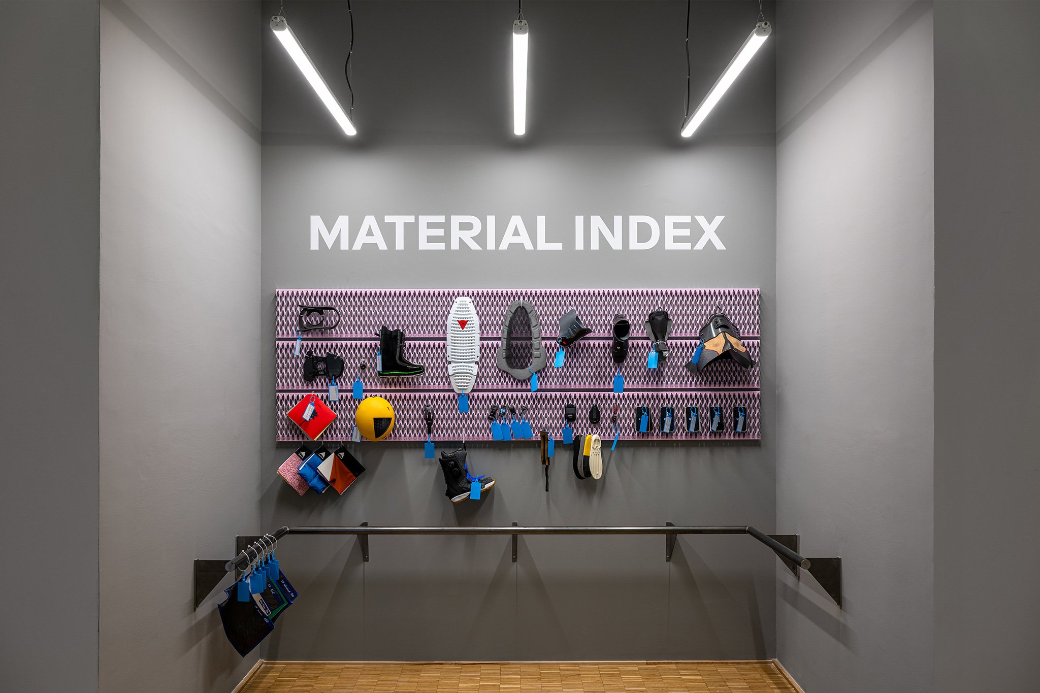 A grey gallery wall in White Out, a Triennale exhibition about winter sports with large text that reads "Material Index" featuring a selection of outdoor equipment produced in various materials.