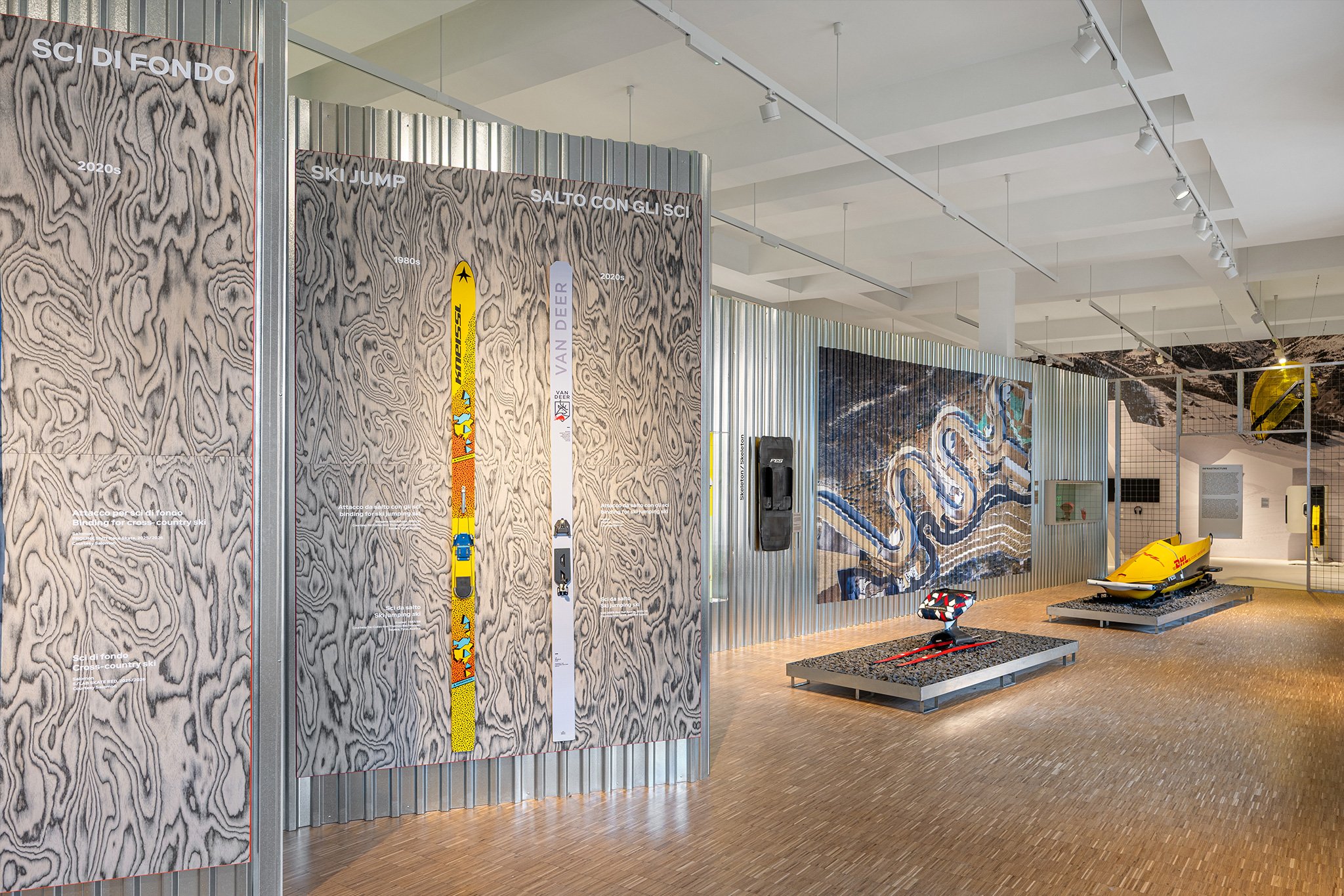 Two skis — one retro and one current — are shown on a wood panel installed on a corrugated steel wall in the Triennale winter sports exhibition White Out.