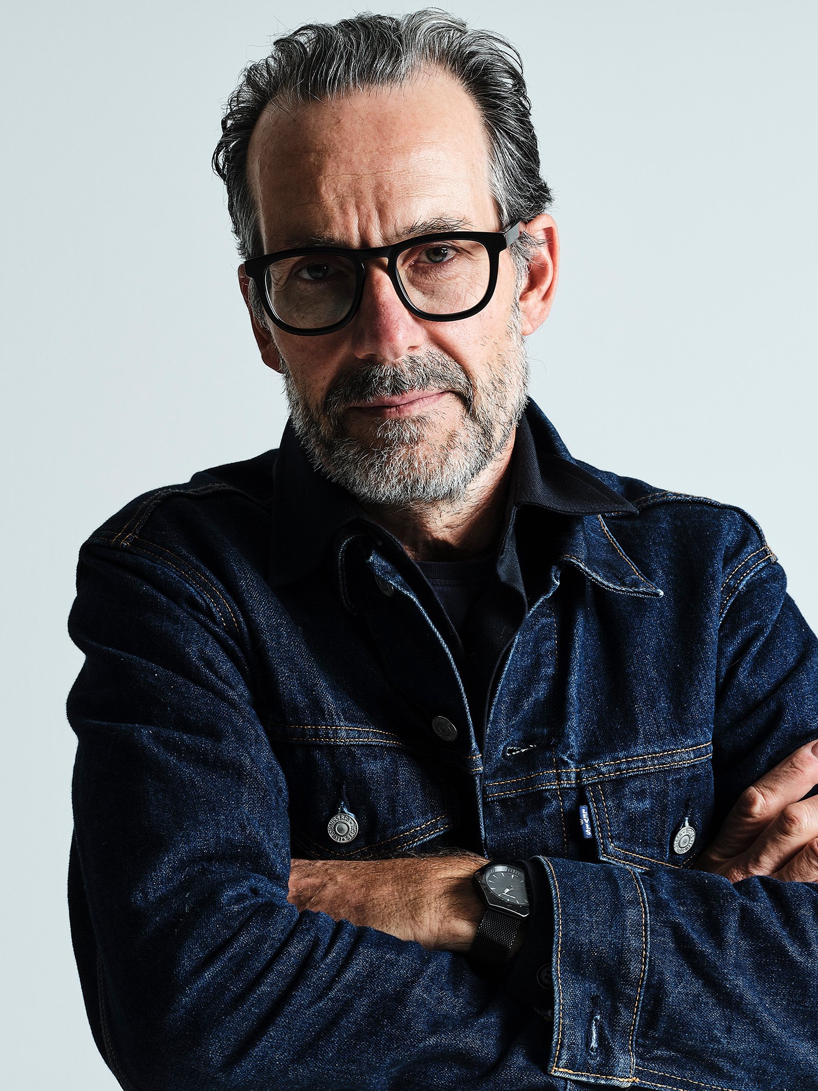 A portrait of Triennale White Out curator Konstantin Grcic wearing a dark denim jacket and black glasses.