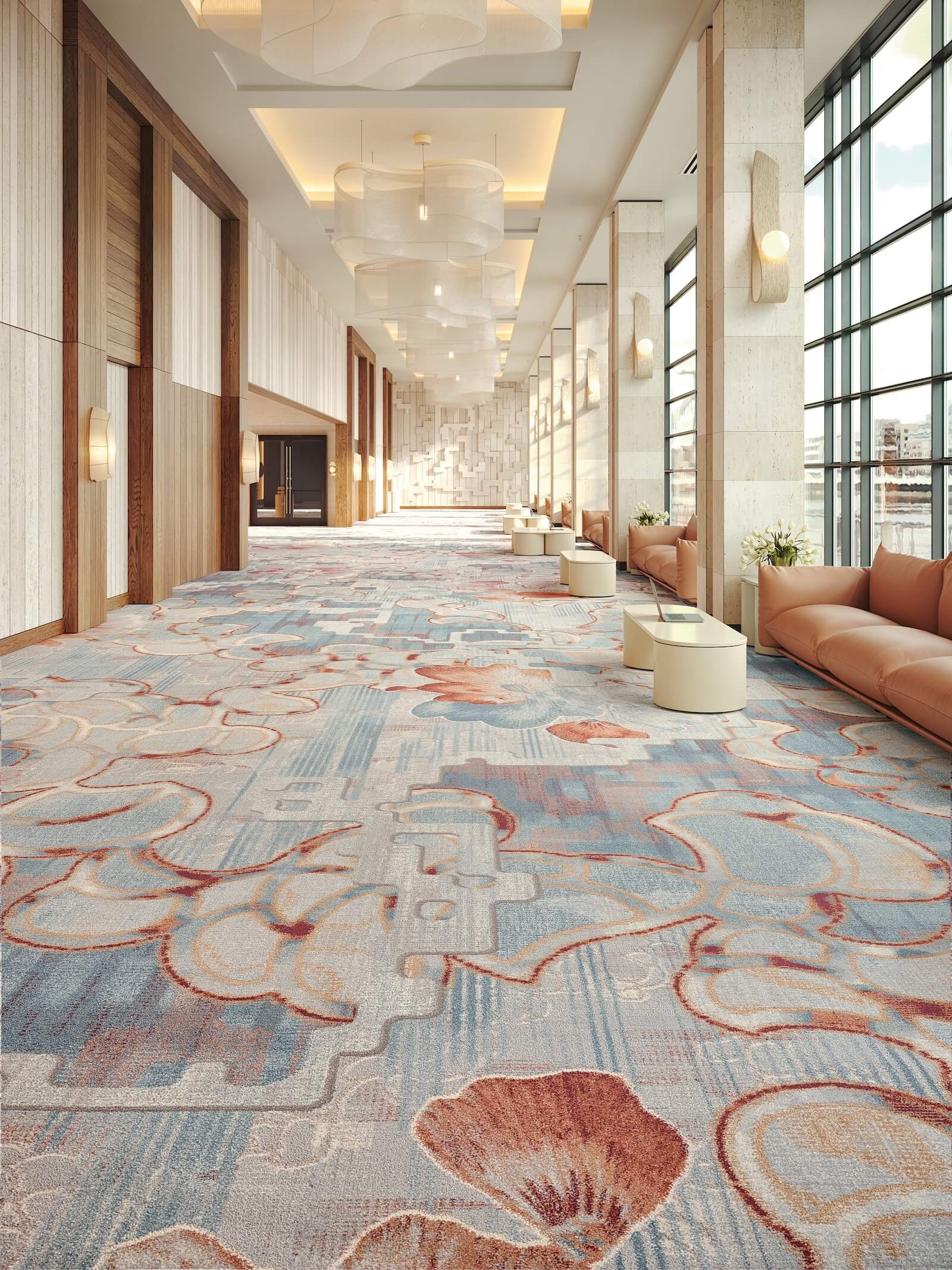 Spacious, modern hallway with patterned carpet, tan leather seating, round tables, large windows, and soft overhead lighting.