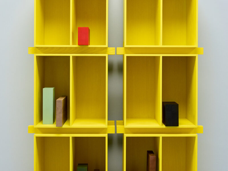 Two yellow shelving units, each with four compartments, display colorful rectangular blocks arranged in various positions on the shelves.
