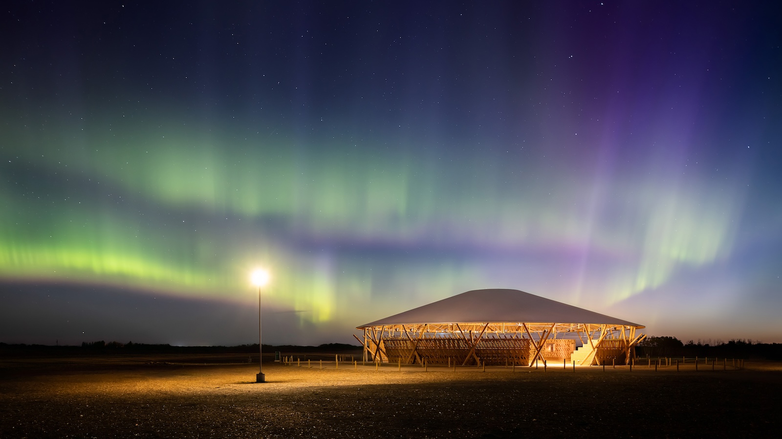 A wooden pavilion lit at night with aurora borealis displaying green and purple lights in the sky above, evoking the enchanting atmosphere often celebrated at the Governor General's Awards.