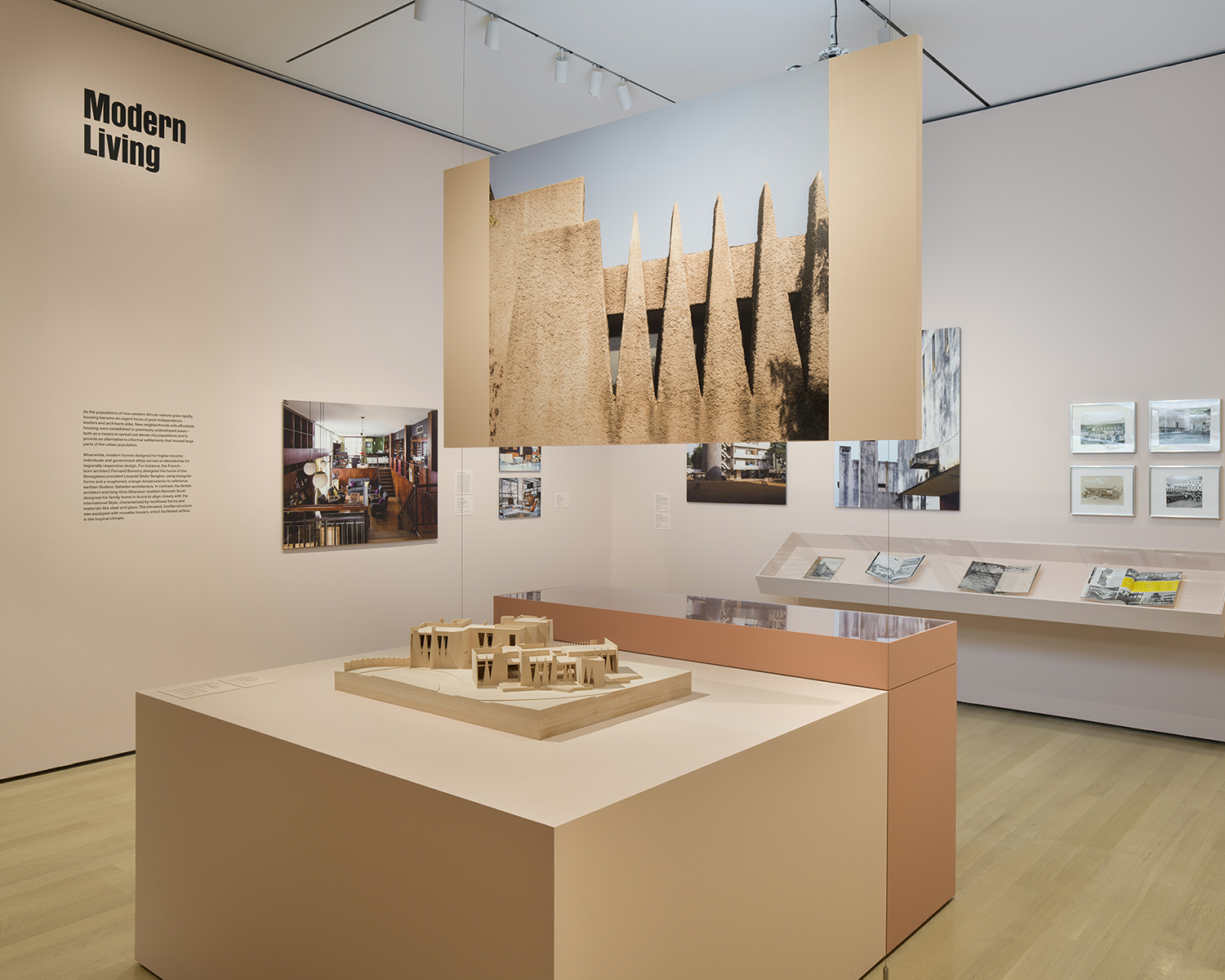 Exhibit room titled "Modern Living" featuring architectural models, photographs, display cases with books, and wall-mounted images under bright lighting—perfect for exploring during your visit to our July events.