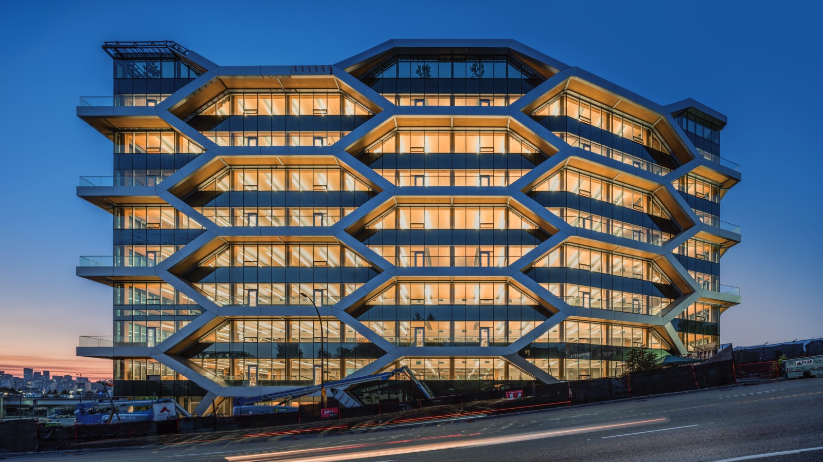 Modern office building with a distinctive hexagonal honeycomb facade illuminated at dusk, featuring large glass windows and multiple floors.