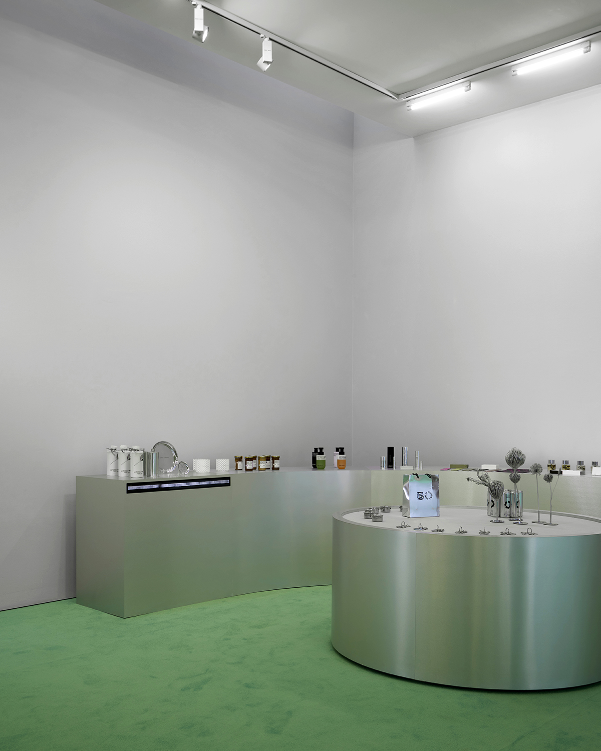 A minimal retail display with metallic counters, various products arranged neatly, and a green carpeted floor under bright ceiling lights highlights special July events.