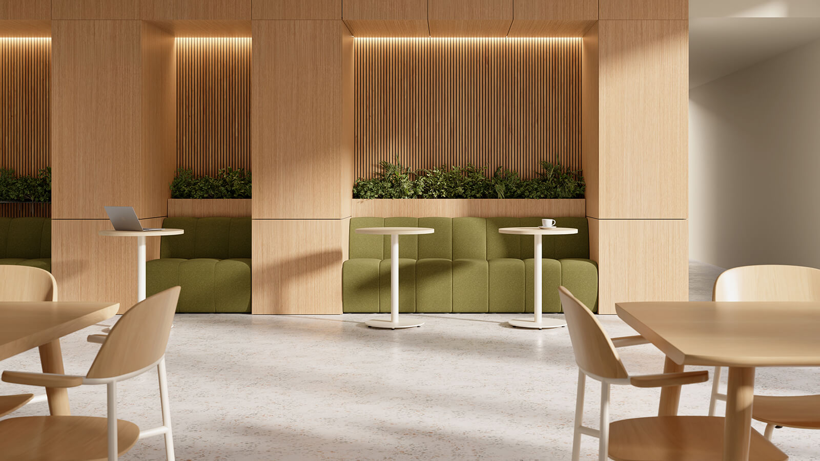 Modern café interior with light wood furniture, green cushioned seating, Keilhauer modular seating, white tables, plants, and a laptop and cup on separate tables. Natural light enters from the right.