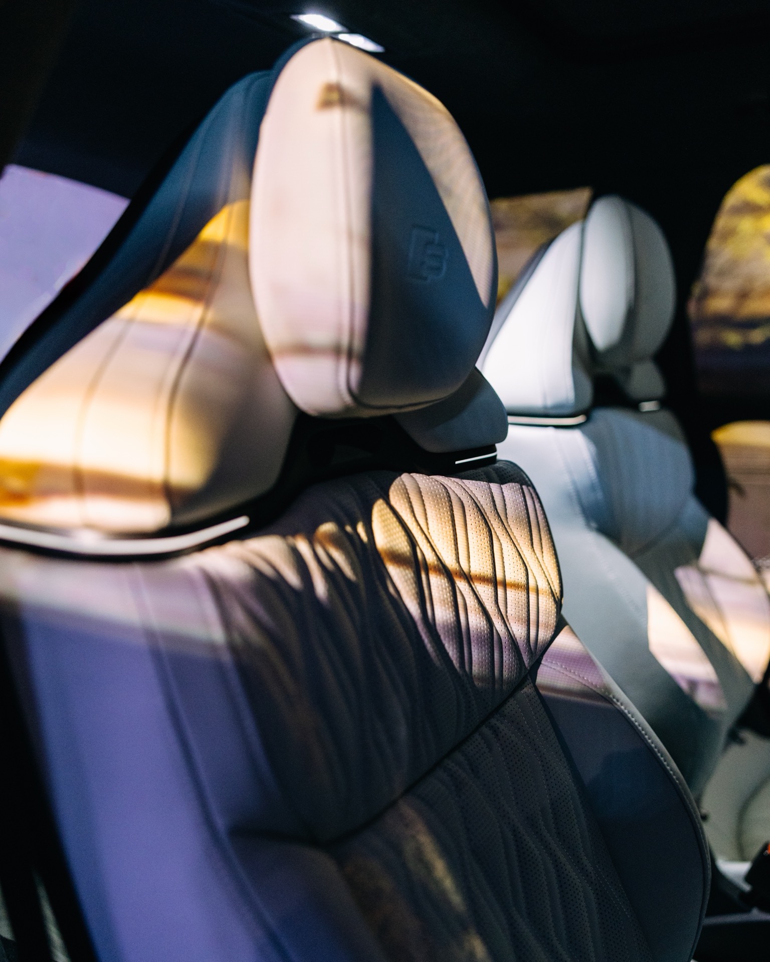 Front car seats of an Audi Q9 with light patterns cast across the headrests and upholstery.