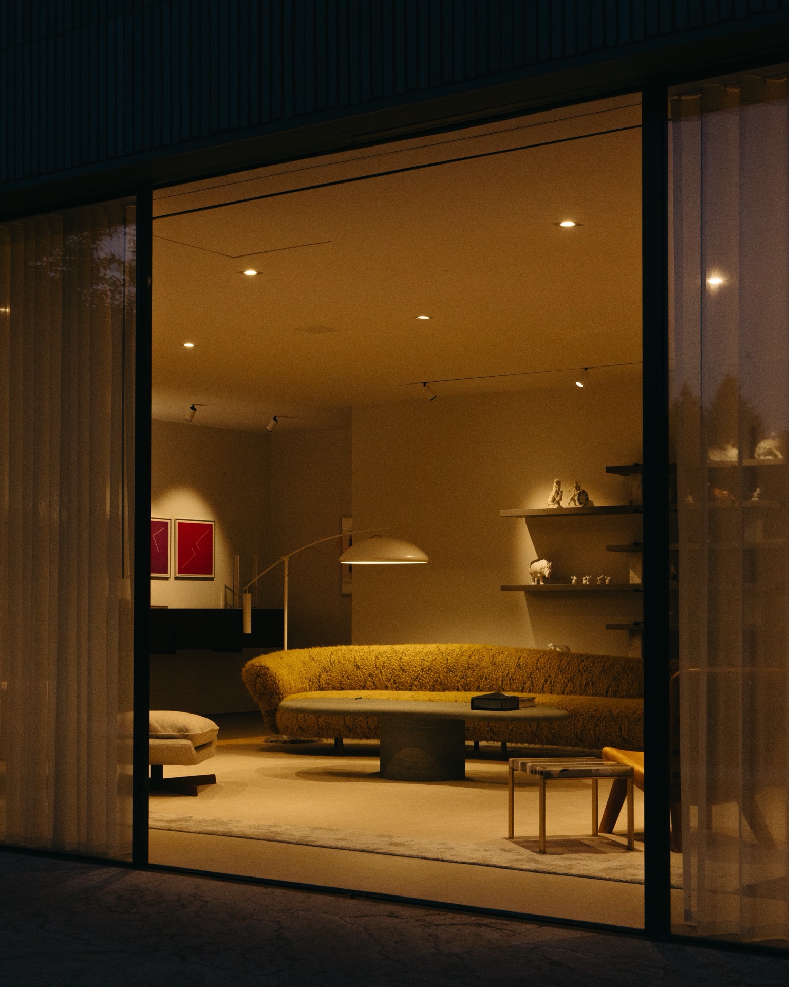 A modern living room viewed through Audi Q9 sliding glass doors, featuring a textured yellow curved sofa, a stone coffee table, and recessed ceiling lighting.