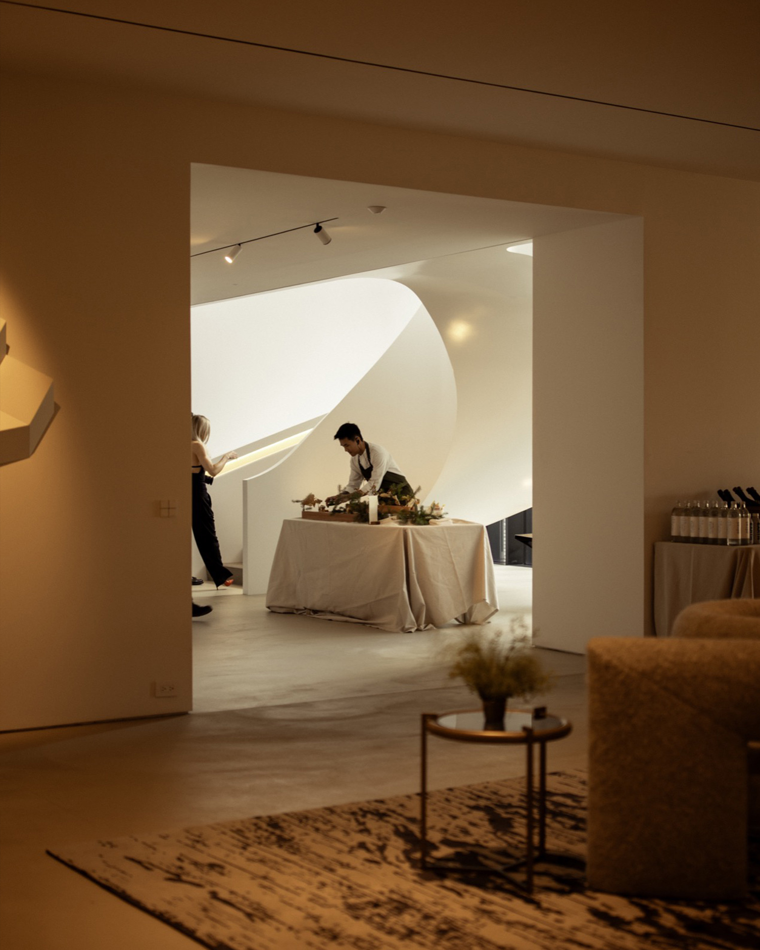 A person prepares food at a table in a bright, modern interior viewed through an arched Audi Q9 doorway.