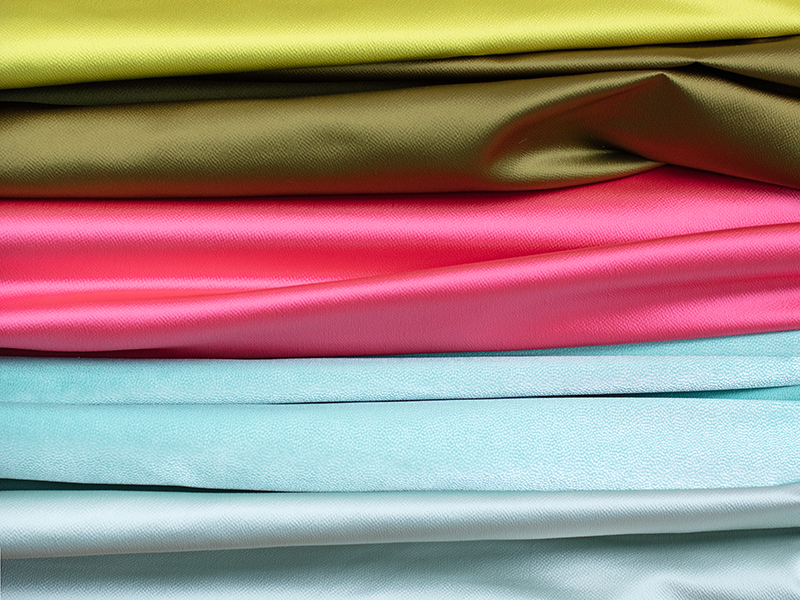 A stack of folded fabric in layers of lime, olive, hot pink, light blue, and pale silver.