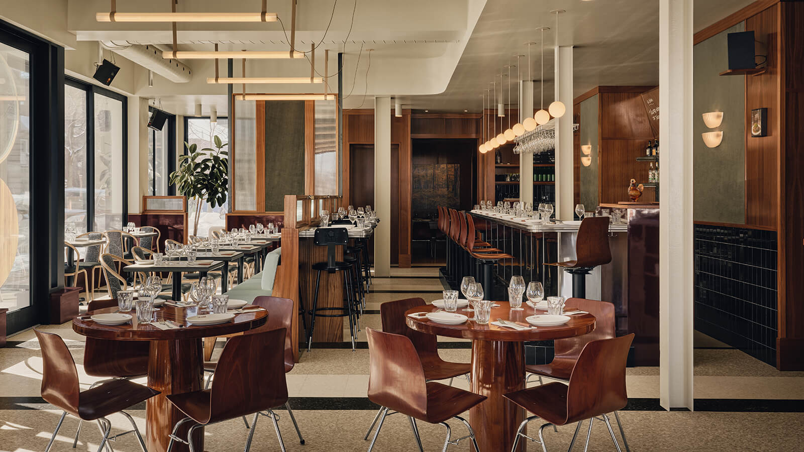 Restaurant interior in Montreal featuring wooden tables, curved chairs, and a bar with stools under globe pendant lights.