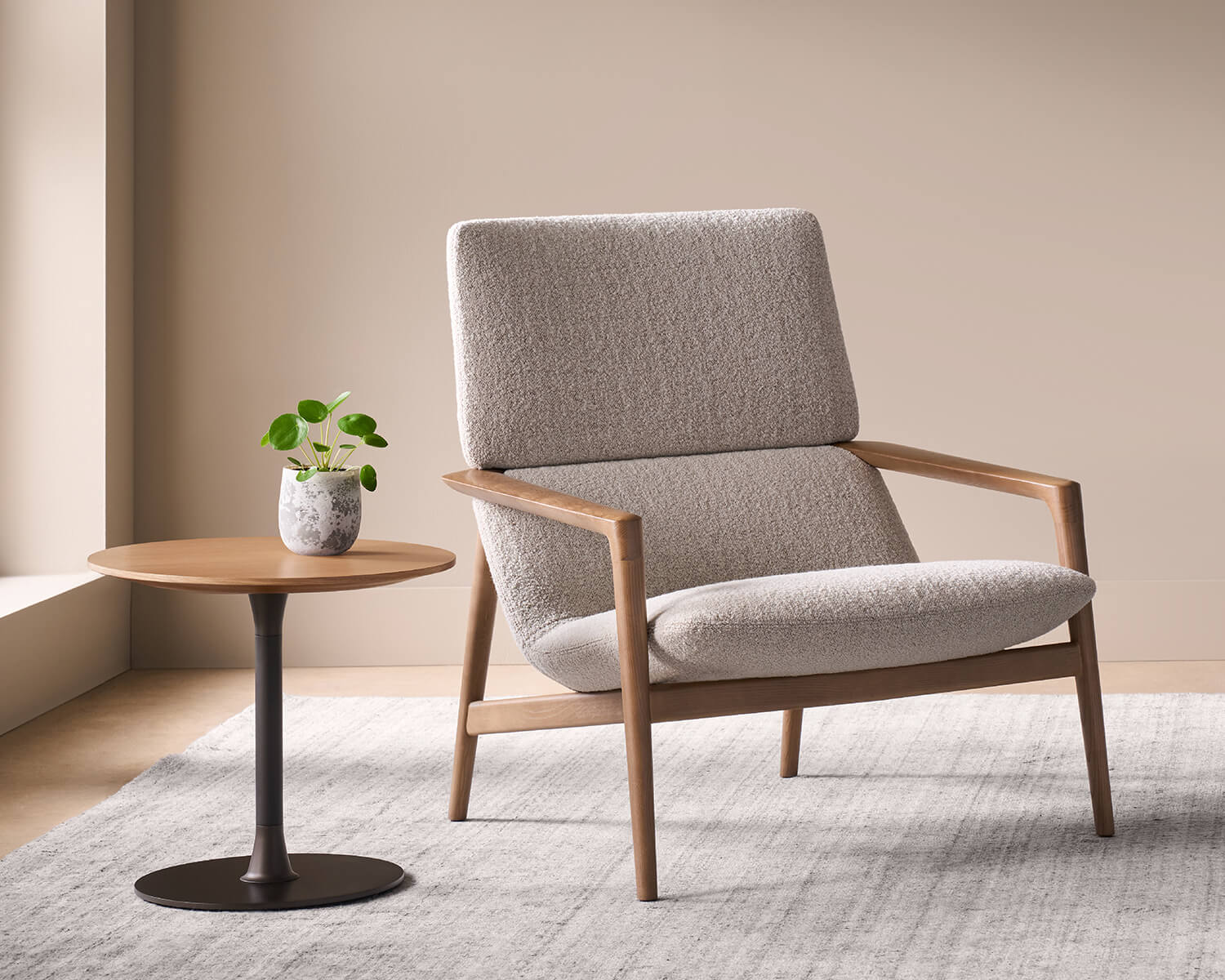 A Solenne upholstered armchair with a wooden frame sits next to a small round side table with a potted plant.