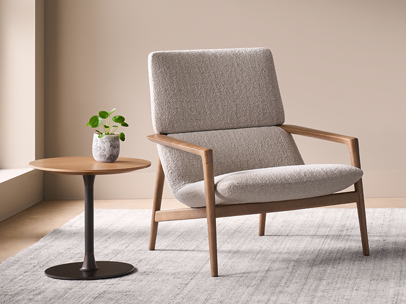 A Solenne light grey upholstered armchair with wooden arms sits next to a small round side table with a potted plant.