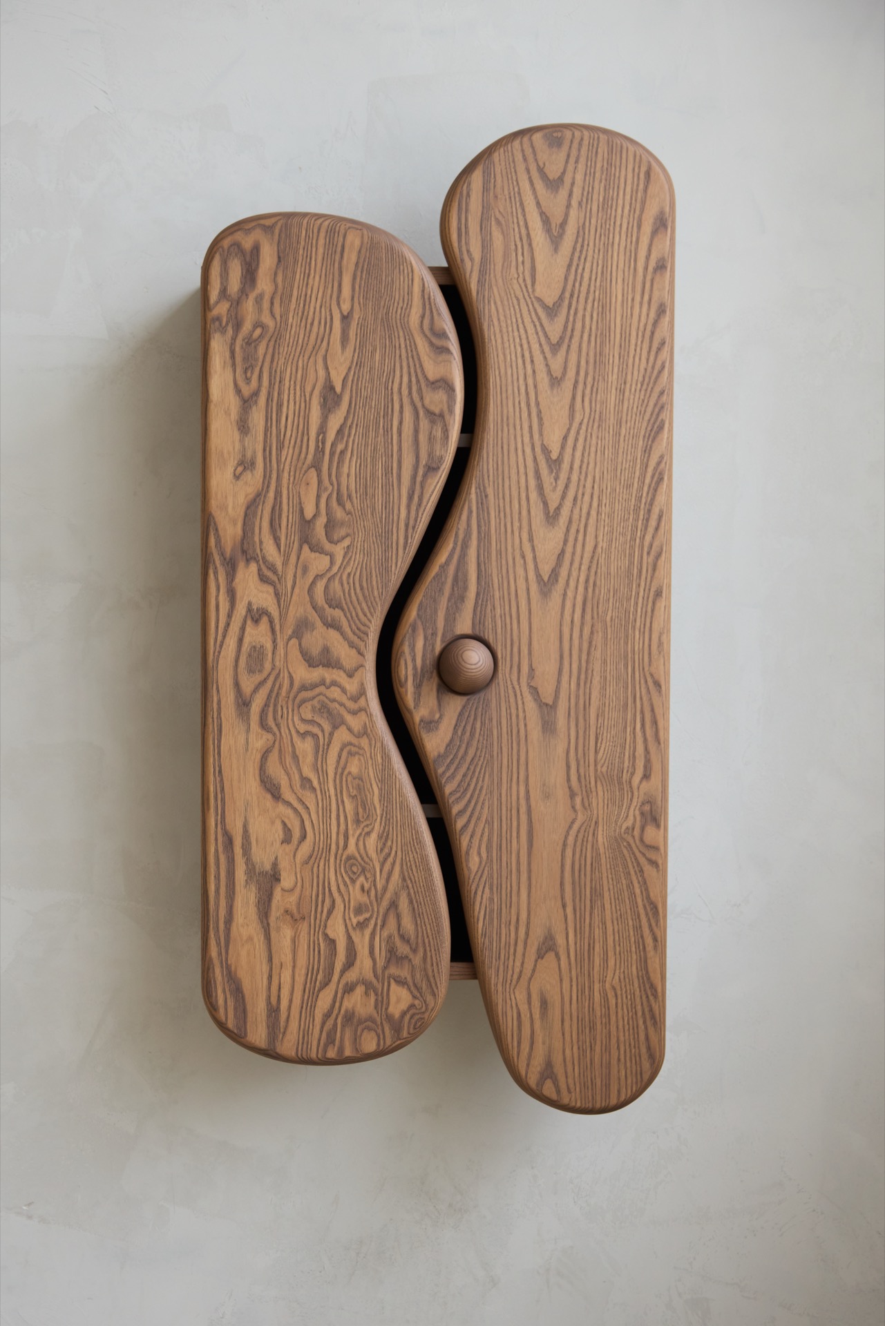 Wooden wall-mounted cabinet with two curved doors and a single round knob, featuring a prominent wood grain pattern.