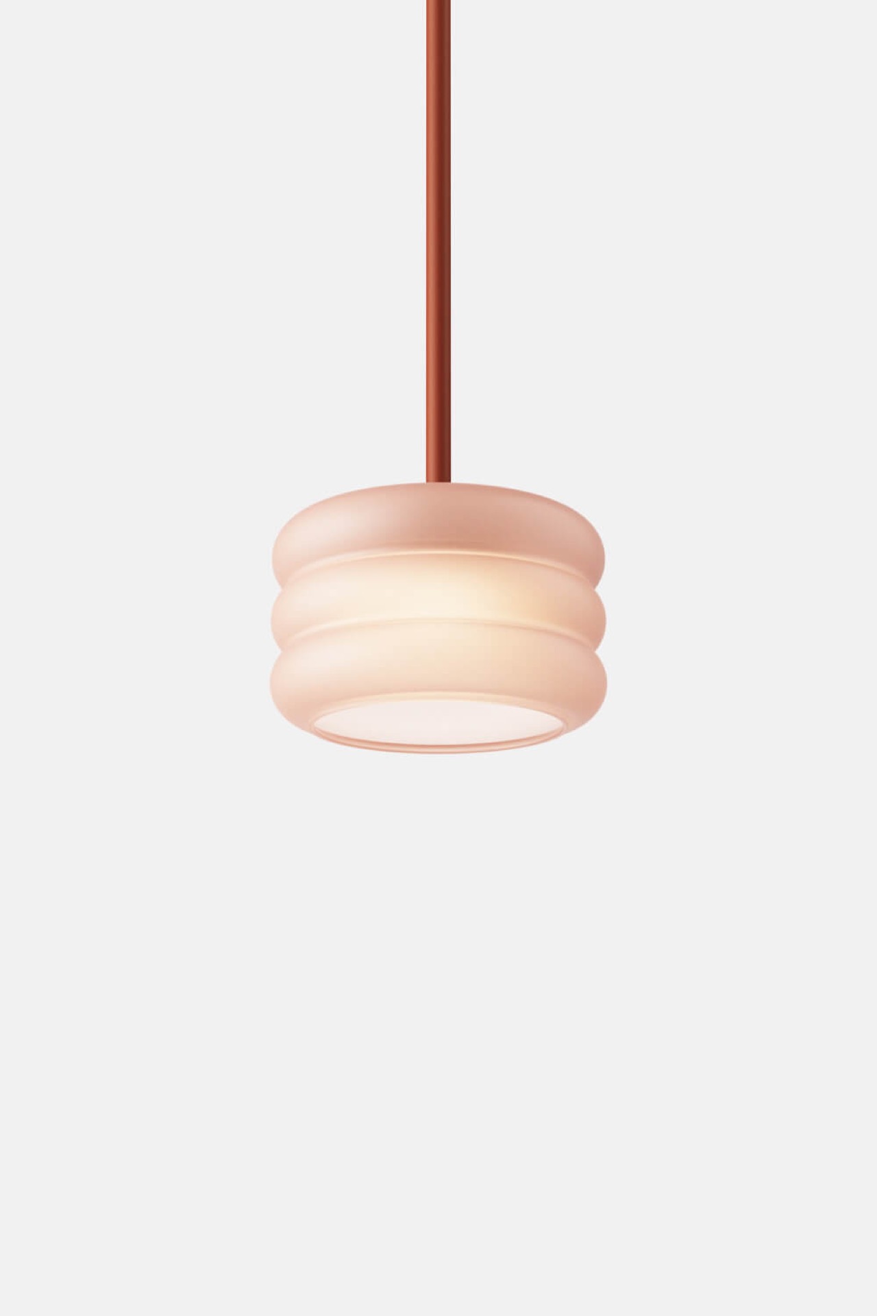 A round, pink pendant light with a ribbed design hangs from a thin rod against a plain white background.