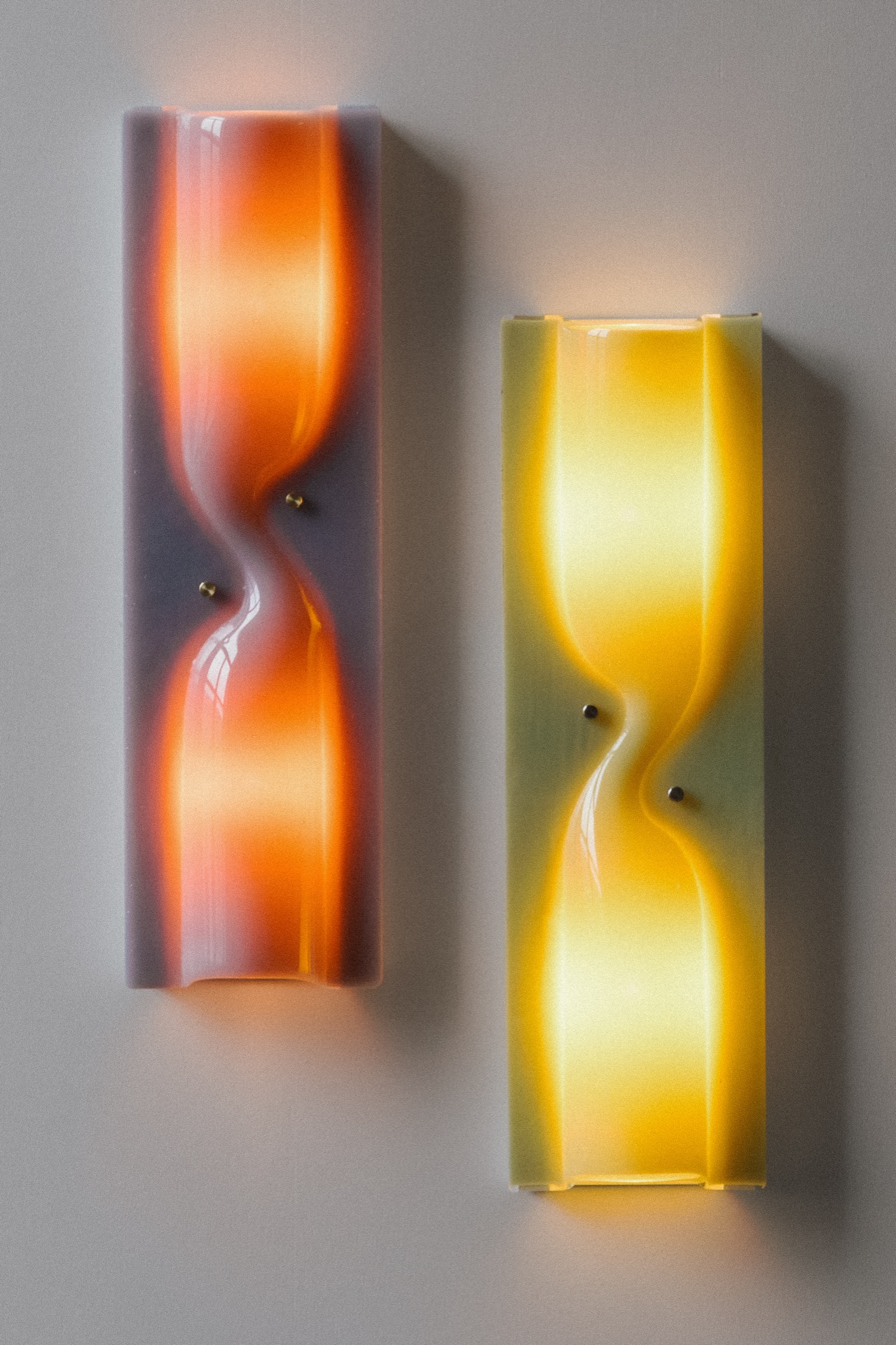 Two rectangular wall sconces with curved, hourglass-shaped designs emit warm orange and yellow light against a neutral wall.