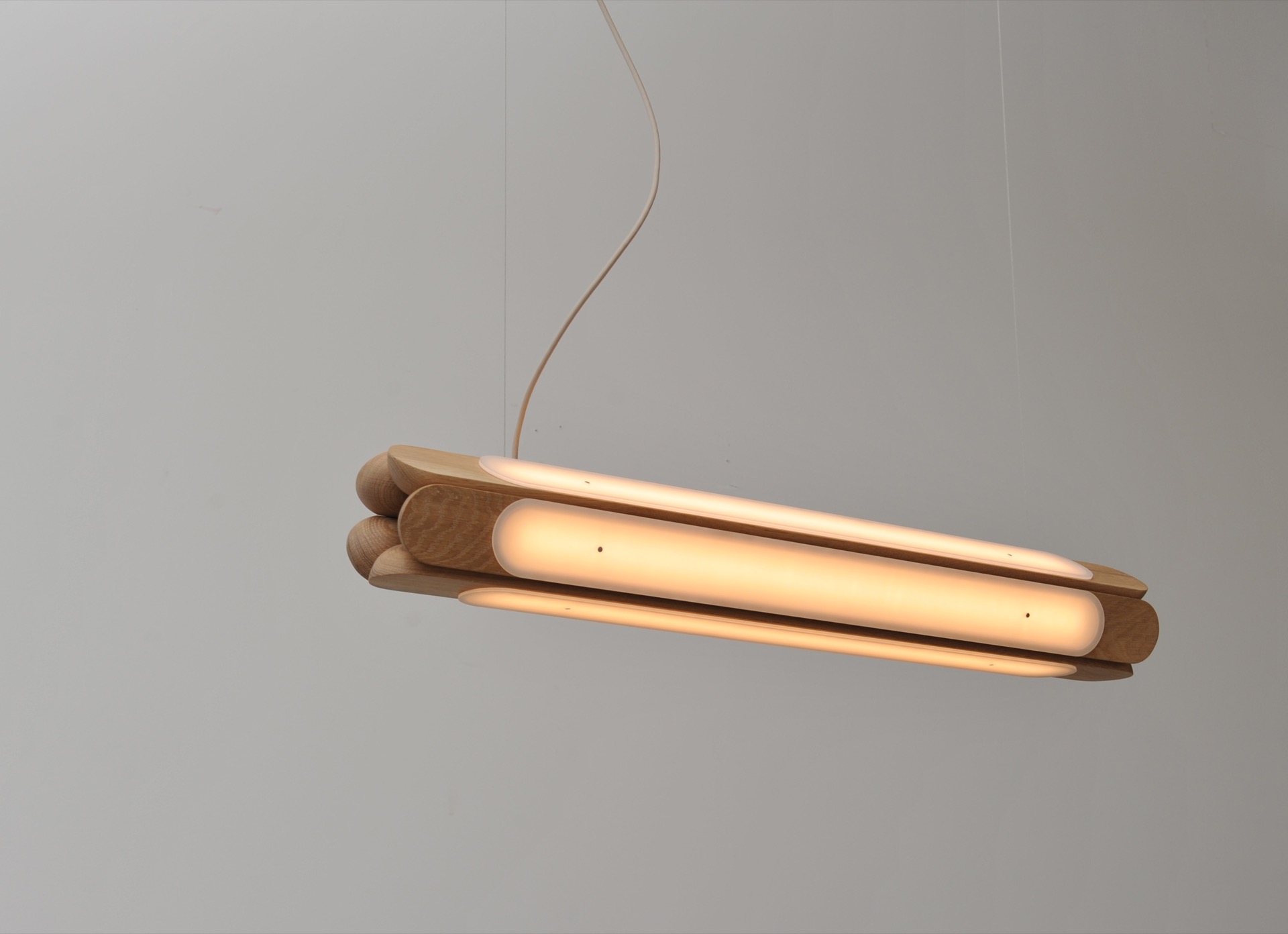 Modern wooden pendant light fixture with rounded edges and integrated LED strip, suspended by a single cord against a plain white wall.